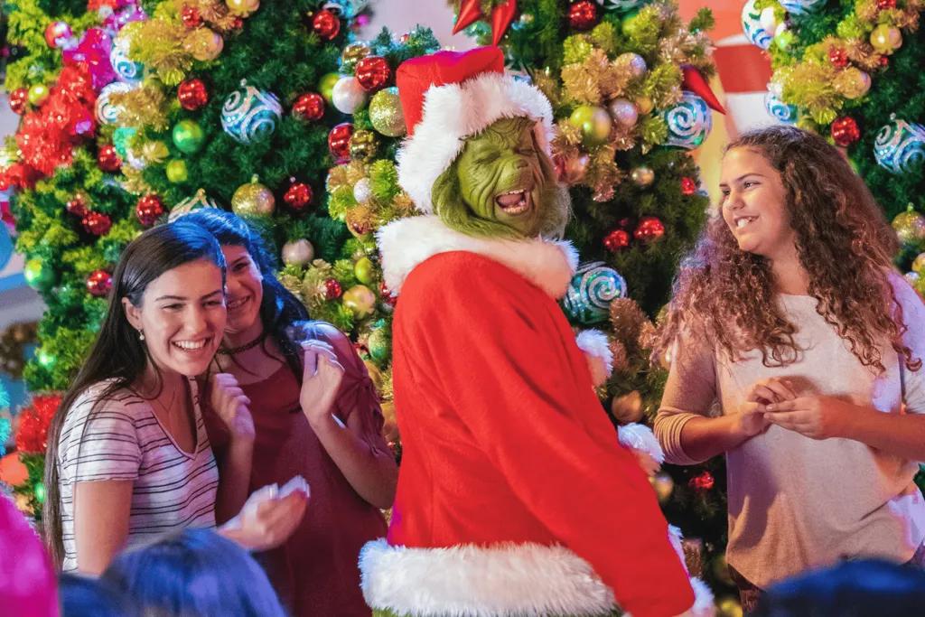 Three girls posing in front of a Christmas tree with the Grinch dressed as Santa
