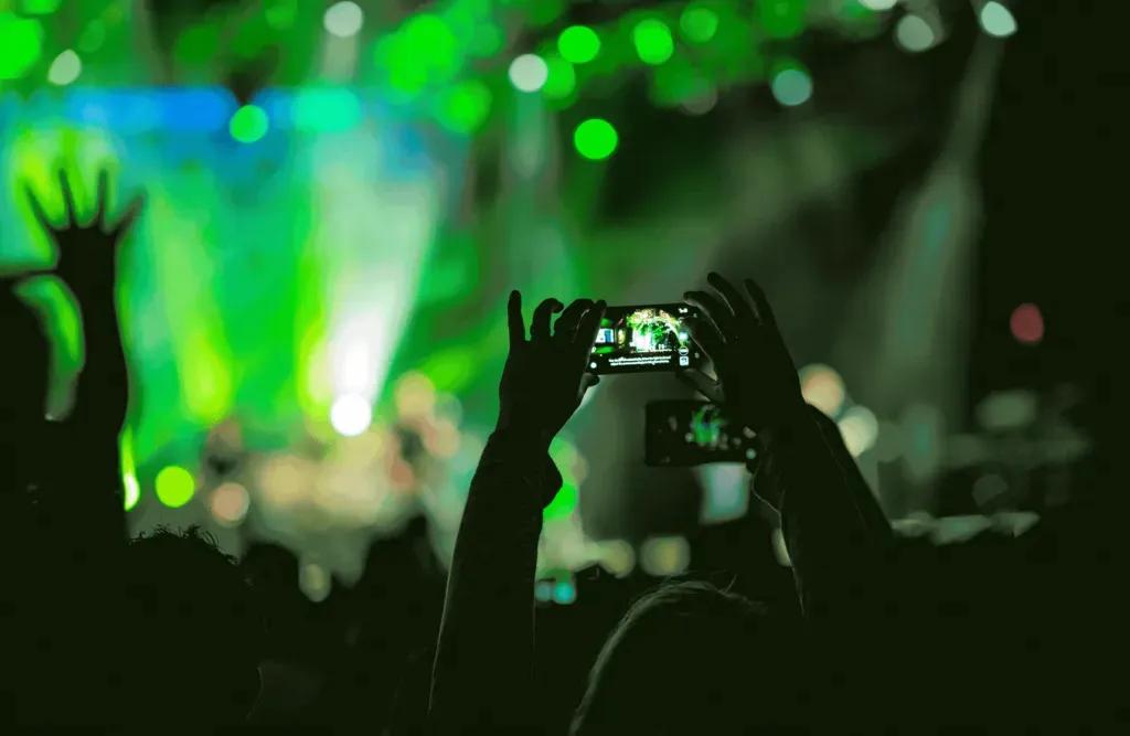 Jemand in der Menge bei einem Konzert hält sein Handy über den Kopf, um ein Foto von der Bühne zu machen