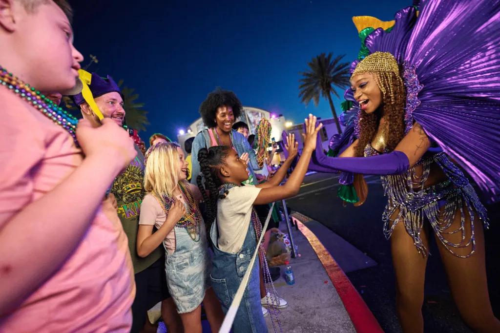 A woman dressed in carnaval costume high fiving a young girl in the crowd