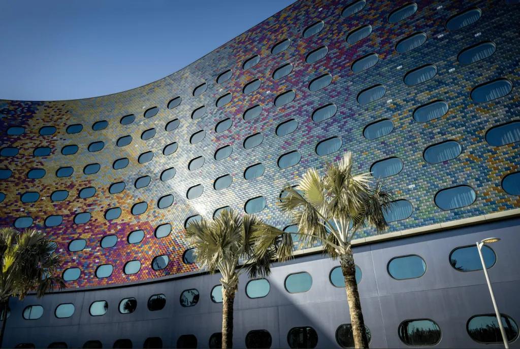 The side of a hotel covered in rounded windows and iridescent tiles