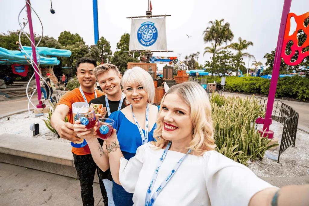 A group of friends taking a selfie with food and drink in front of a Seven Seas Food Festival sign