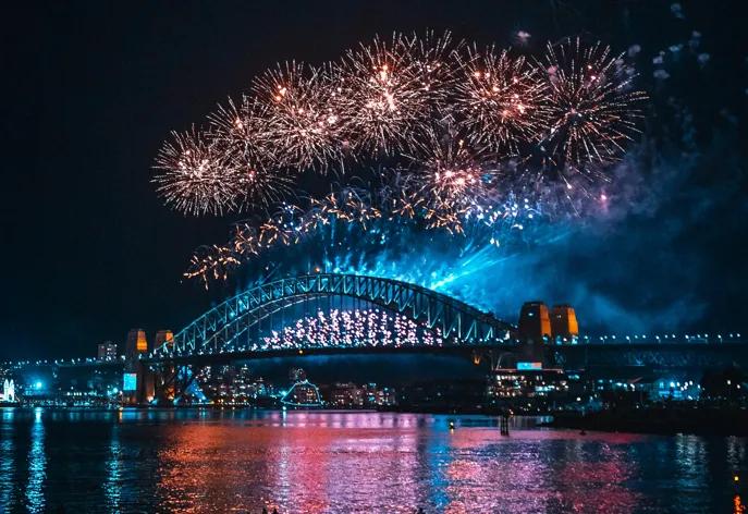 Ein Feuerwerk über der Sydney Harbour Bridge erhällt die Brücke und lässt das Wasser des Hafens rot erleuchten