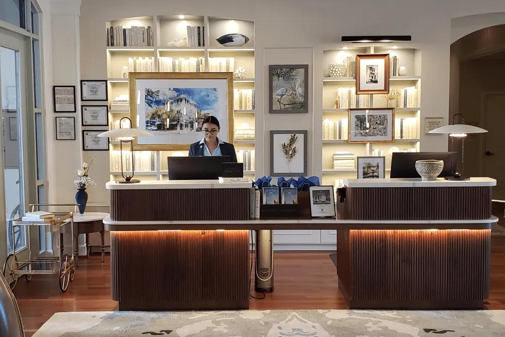 A lobby which is small and clean with two small dark modern desks and one receptionist sat behind them. there are many images on the walls of the old hotel before renovation.