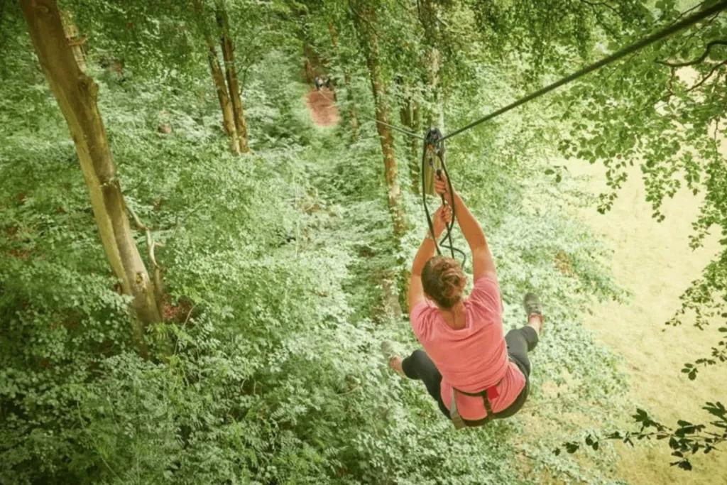 Woman in tree tops zooming down steep zip line that connects to the floor. 