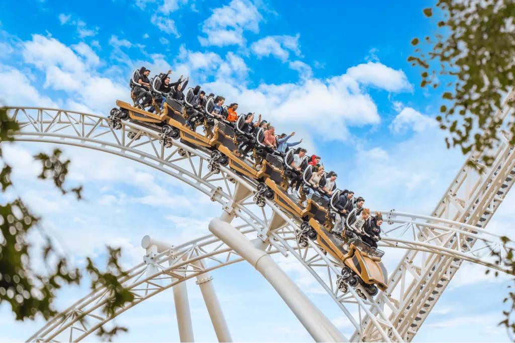 Large golden rollercoaster car heading down steep fall on white track.
