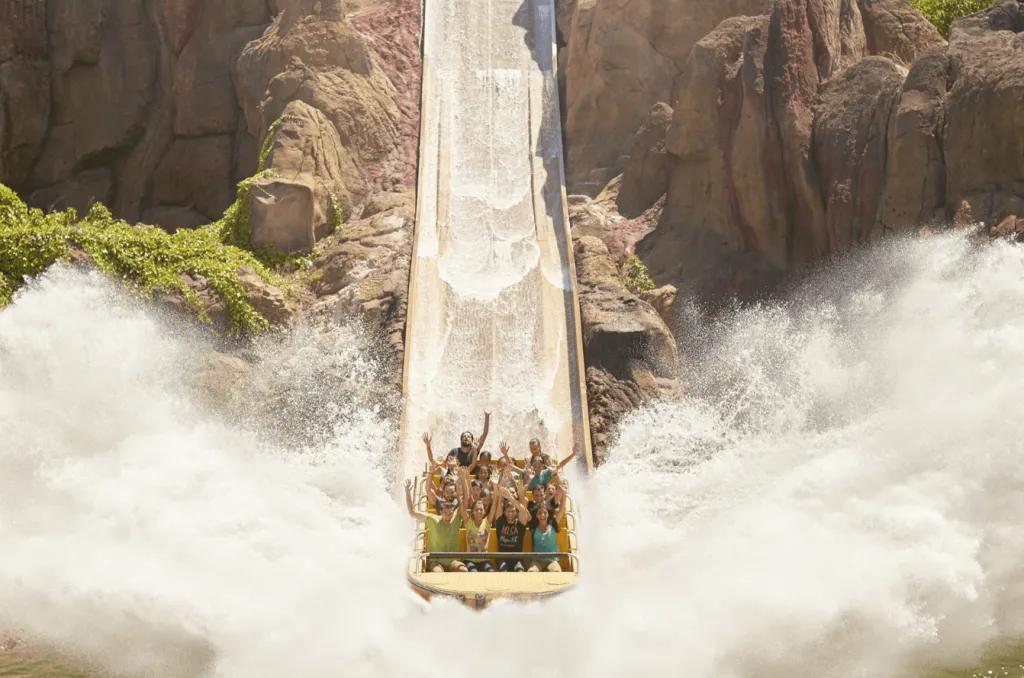A boat at the bottom of the drop of a water ride making a large splash