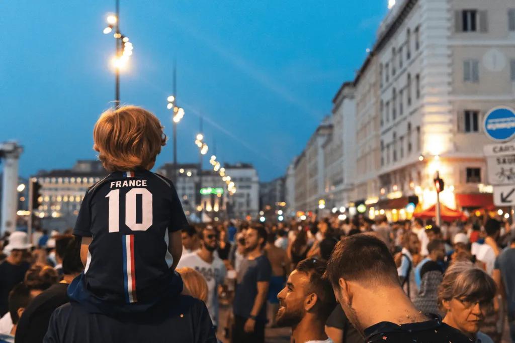 Football fans in a European city with one child on his dads shoulders wearing a football shirt with 10 on it.