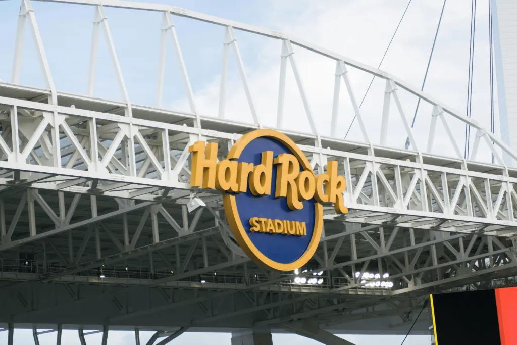 A tall metal structure, which is the top of the Had Rock Stadium. There is also a yellow and blue sign saying "Hard Rock Stadium".