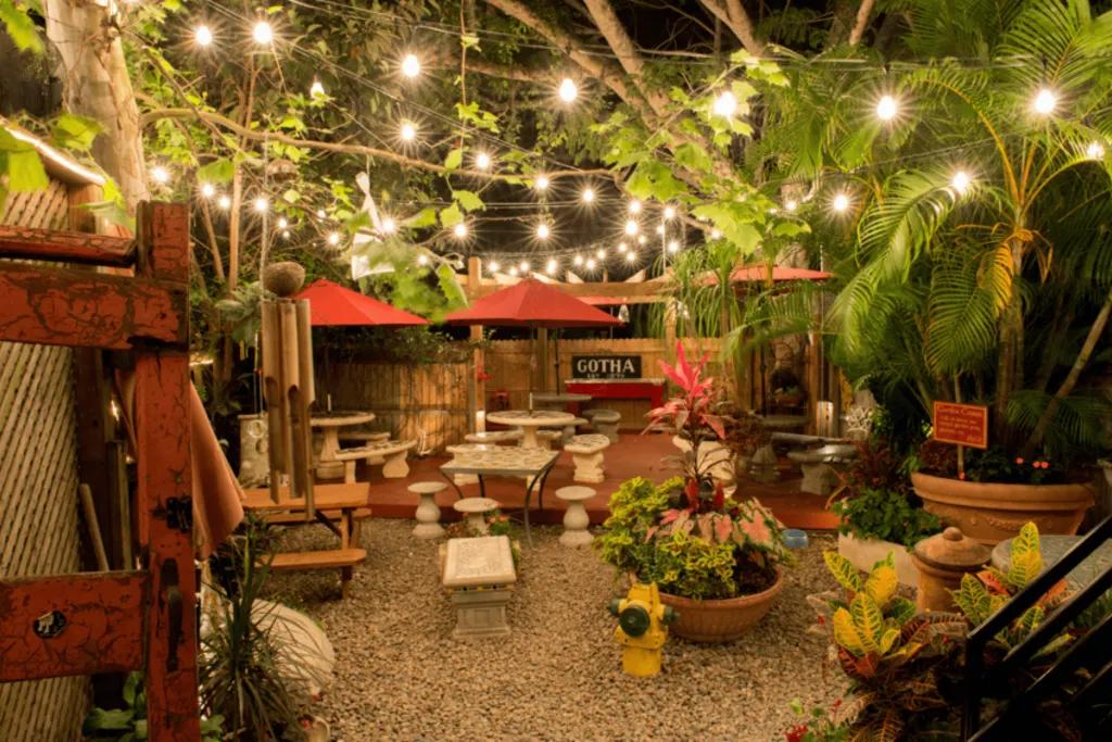 Vibrant patio with leaves and plants hanging overhead. It is themed like a garden with white stools and benches.