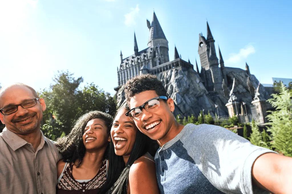 A family laughing and smiling in front of the grey Hogwarts castle, consisting of a mum, dad, son and daughter.