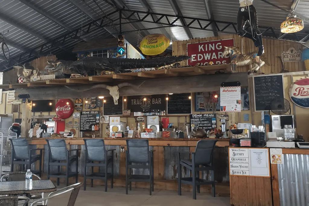 Typical Floridian bar with an old table and many bar stools along. They are different signs of various colours, one says King Edward on it. There is also an alligator on a platform above the bar.