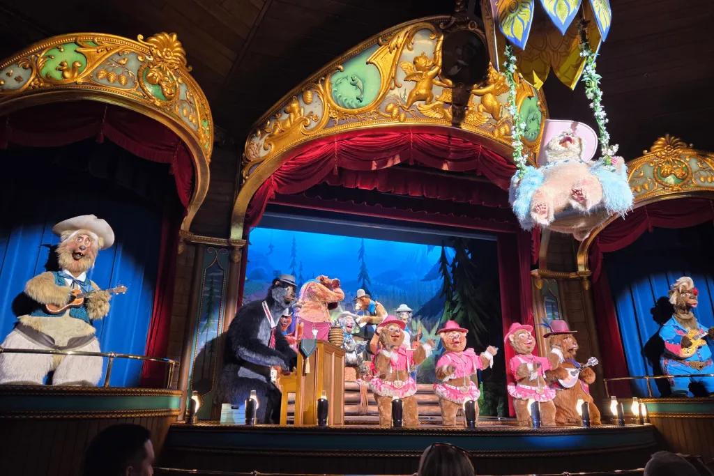 Bears on stage wearing different costumes. One swinging on a swing above the audience.
