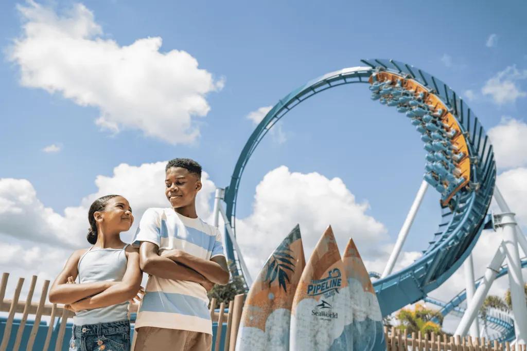Two children posing in front of a surf-themed rollercoaster