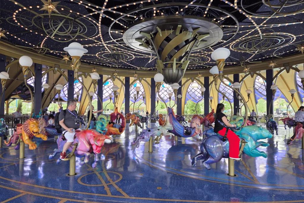 People riding a carousel inside of a beautiful purple ride with star constellations on the ceiling. There are different creatures you can choose to go on, each hand carved.