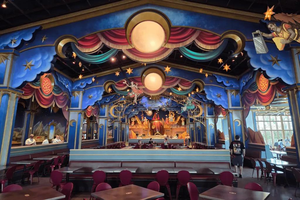 Grand hall with red table and chairs for dining and behind there's a bar and extravagant decorations, featuring stars, planets and more space theming! 