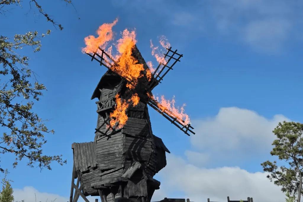 A wooden windmill spinning around with each of its four arms set on fire