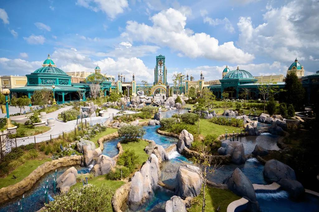 Large garden space with rocks, greenery and small ponds of water. In the background you can see buildings including the Constellation Carousel, as well as the Epic portal.