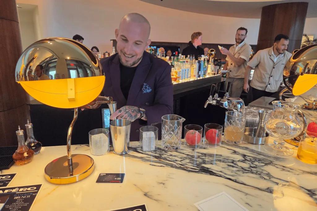 Bartender pouring drinks behind a bar with gold decorations including a large lamp.