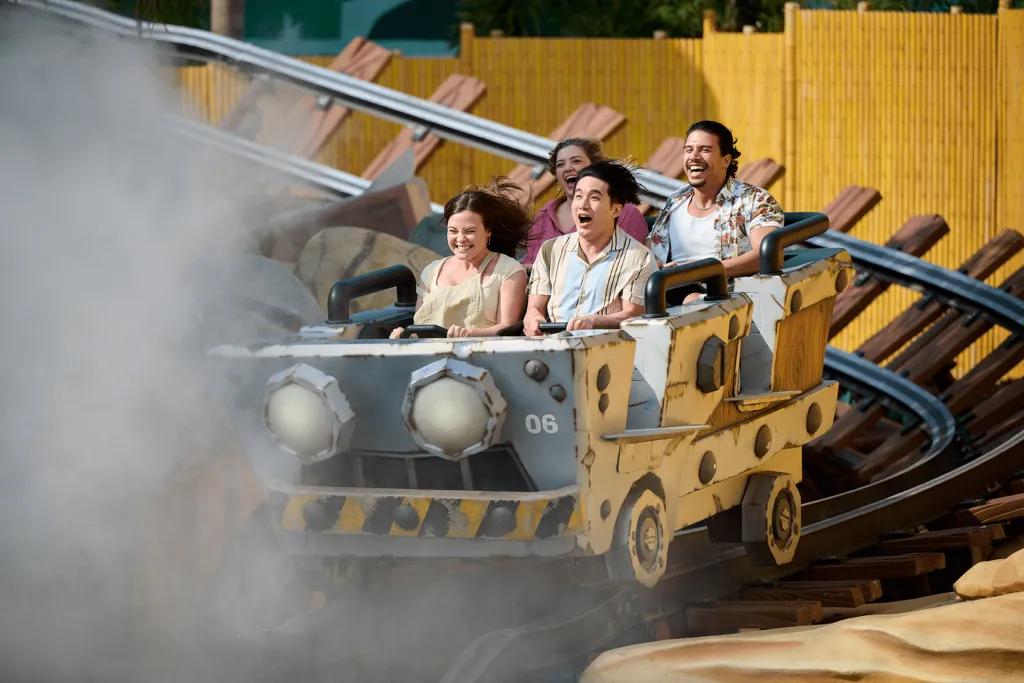 4 people sat in a mine cart shaped rollercoaster car going along a wooden track into a cloud of smoke.