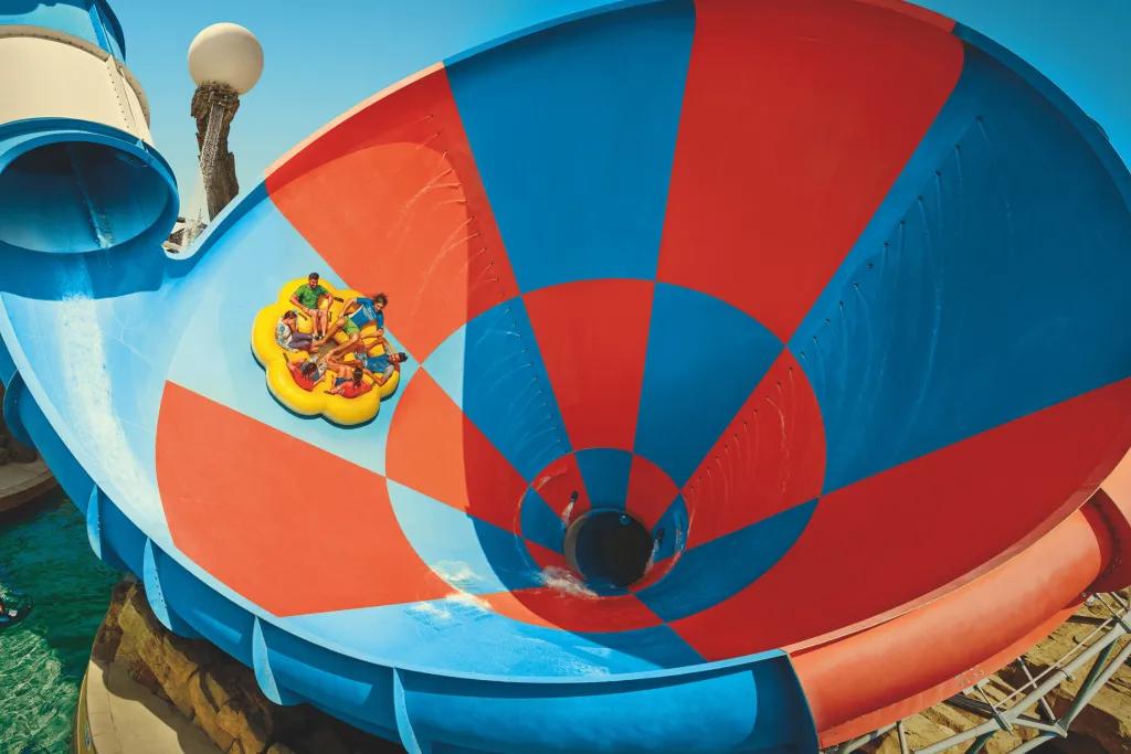 A group of people in a yellow rubber ring dropping down large drop into a funnel water slide.