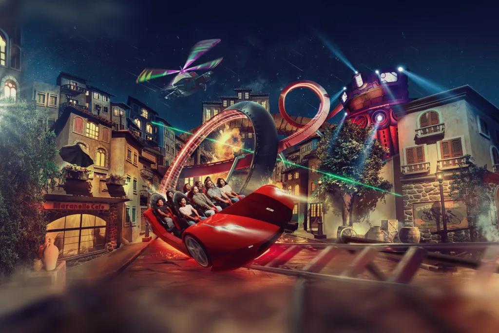 A red simulator styled ride with buildings either side of the track and a helicopter flying overhead. 
