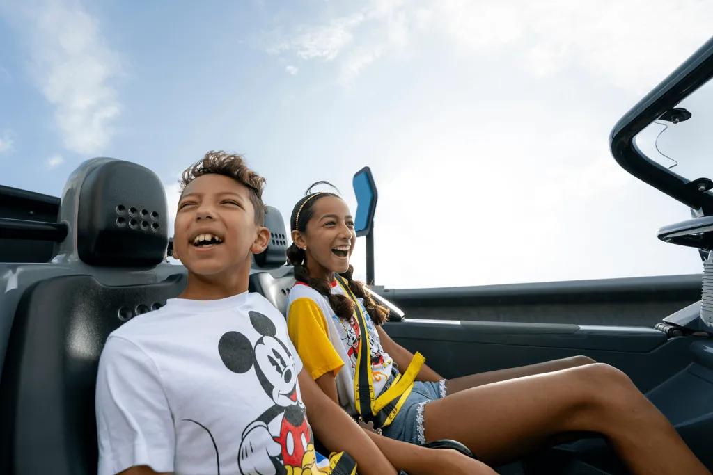 Boy and girl sat on a car shaped rollercoaster vehicle smiling and laughing with joy as they travel at high speeds around a corner.