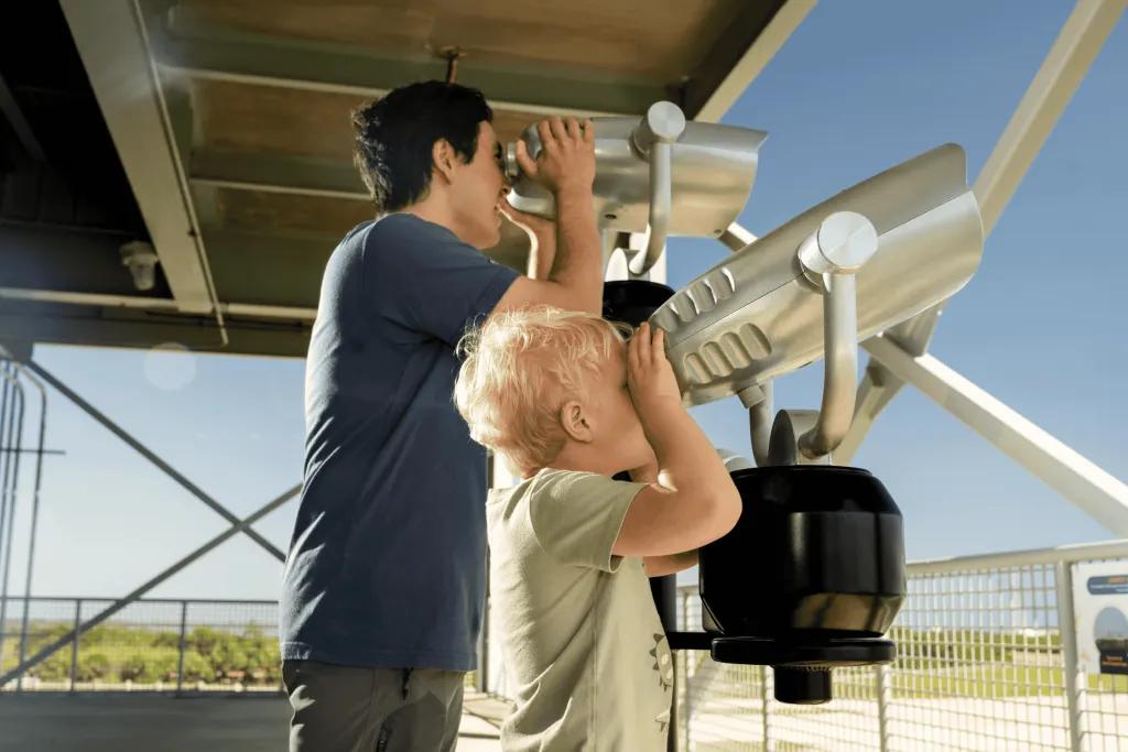 A man and young boy looking into the distance through binoculars