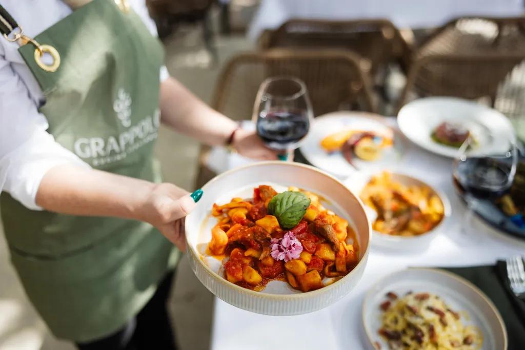 A waiter holding a plate of pasta and a glass of wine