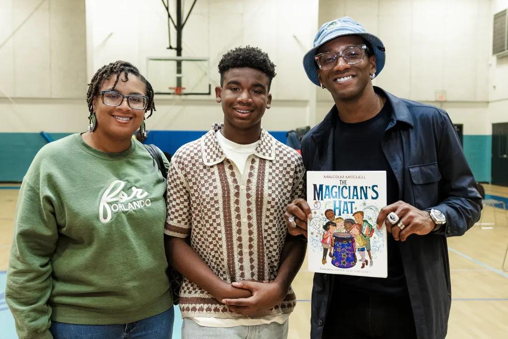 Three people smiling at the camera, one holding a children's book