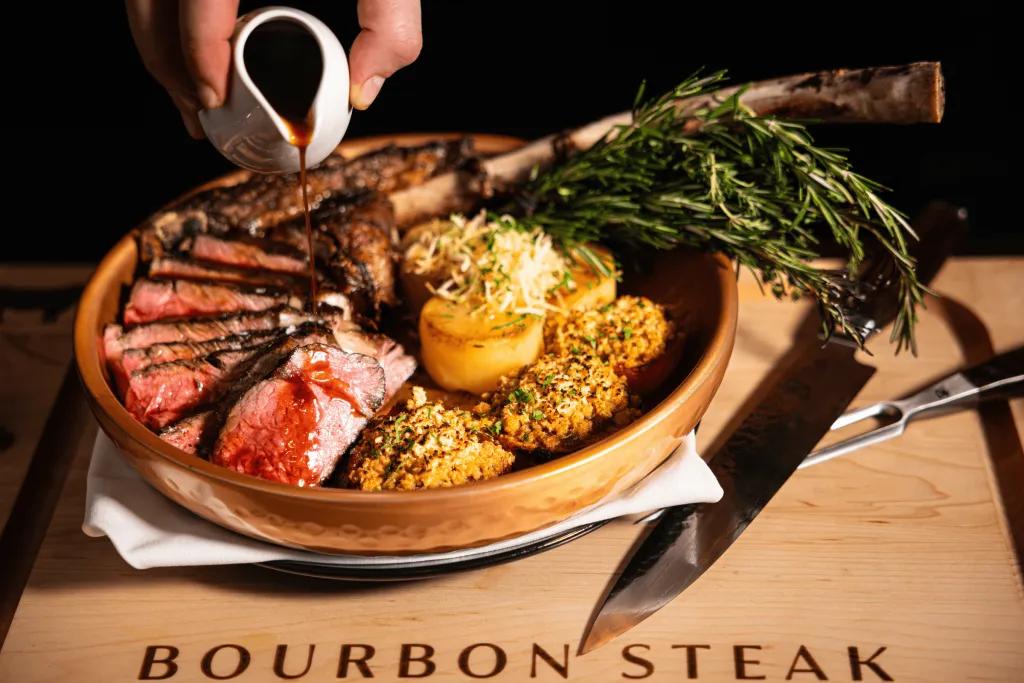 Wooden bowl full of steak cooked medium rare with potatoes and some vegetables.