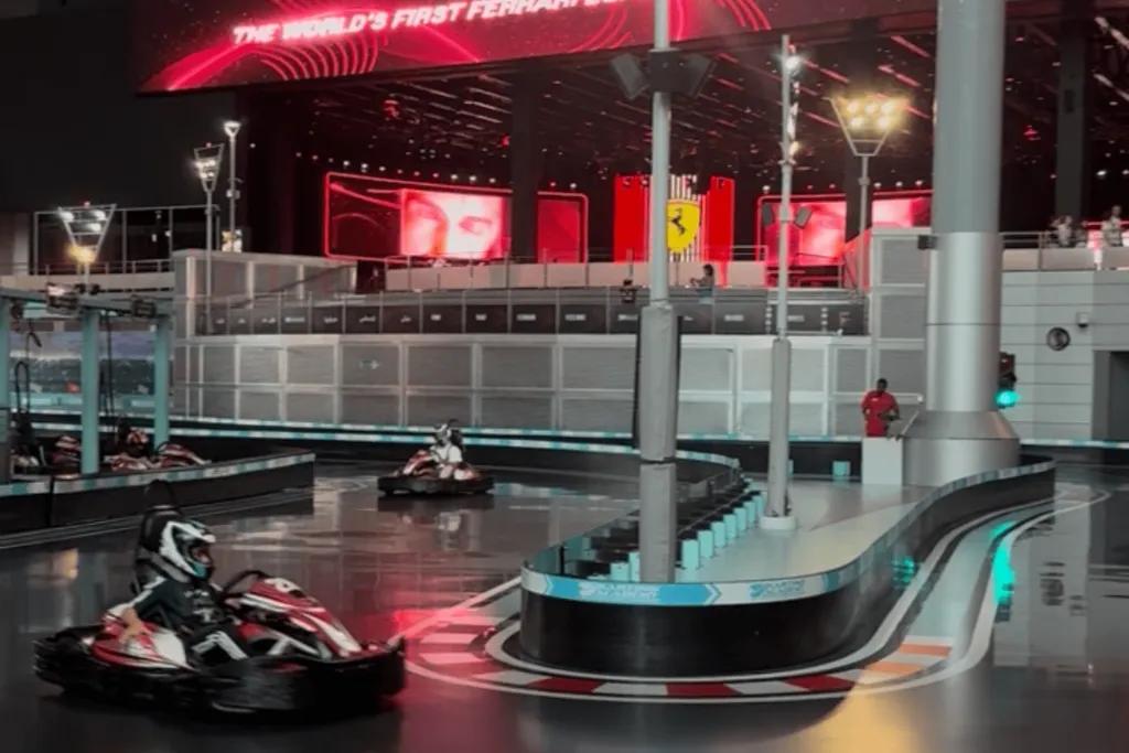 Go karts racing around an indoor track with a large Ferrari sign in the background.
