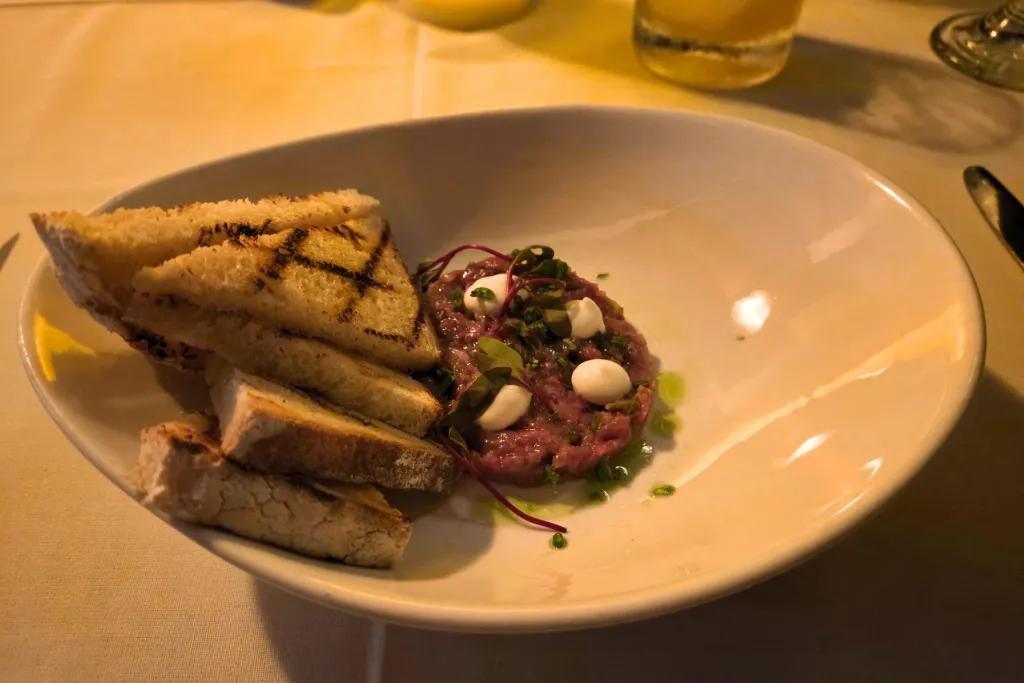 Circular slice of beef with white sauce on top and triangular slices of bread on the side