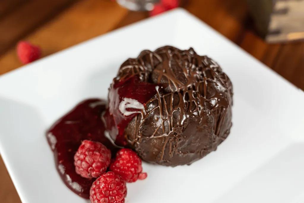 A small chocolate bundt cake on a plate with a raspberry and cranberry sauce
