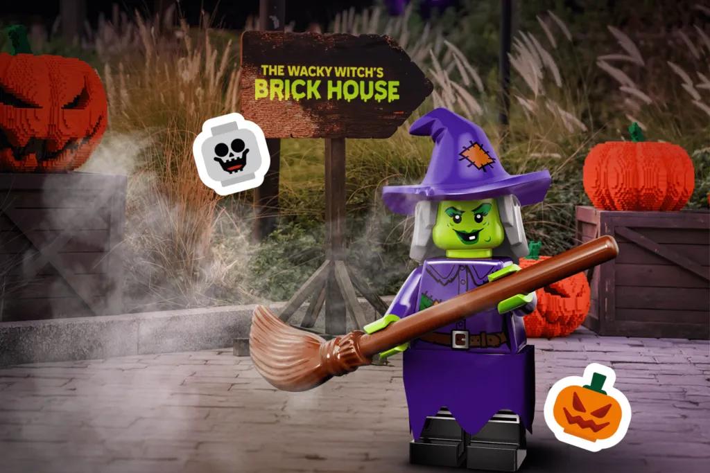 Green witch lego character stood with broom stick by a sign saying - The Wacky Witch’s Brick House. There are also lego pumpkins behind.