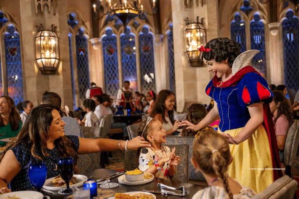 Snow White interacting with a smiling young girl and her mother during a Character Dining experience at Walt Disney World.