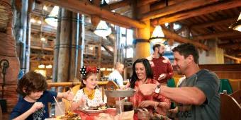 Two adults and two children sat around a wooden table eating barbecue food including ribs and mashed potato