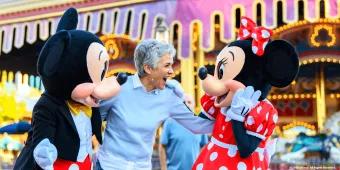 An older woman smiling with Mickey and Minnie