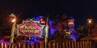 The sign for Tiana's Bayou Adventure lit up at night in front of the attraction