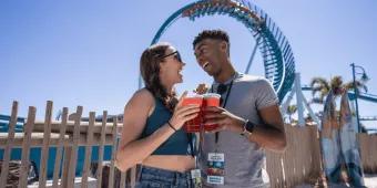A couple posing with drinks in front of the Pipeline rollercoaster at SeaWorld