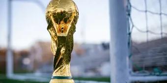 A gold trophy with a globe at the top and things wrapping around it sat in front of a white football goal.