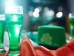 A glass full of green liquid next to a green hat with a shamrock and an Irish flag