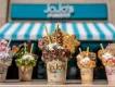 5 large milkshakes topped with cream, marshmallows, candy floss and sprinkles, in front of  sign reading JoJo's ShakeBar