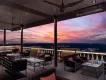 A terrace with sofas, tables and chairs looking out over a purple and pink toned sunset