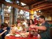 Two adults and two children sat around a wooden table eating barbecue food including ribs and mashed potato
