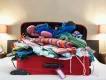 A red suitcase on top of a bed overflowing with clothes 
