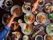 A table full of plates of food with people reaching over to take food with chopsticks