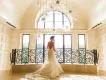 A woman in a wedding dress standing in front of a large window at the top of a grand staircase