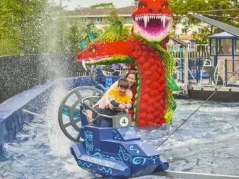 A woman and child getting splashed in a boat ride vehicle in front of a giant Lego sea serpent 