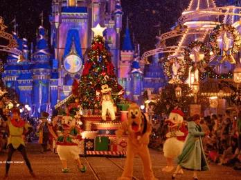 Mickey Mouse standing in front of a Christmas Tree on a parade float. Characters such as Peter Pan, Donald Duck and Pluto dance in front of it