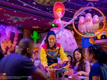 A server bringing a basket full of food to a table of 2 adults and 2 children. There is Toy Story theming in the background including a figure of Bo Peep